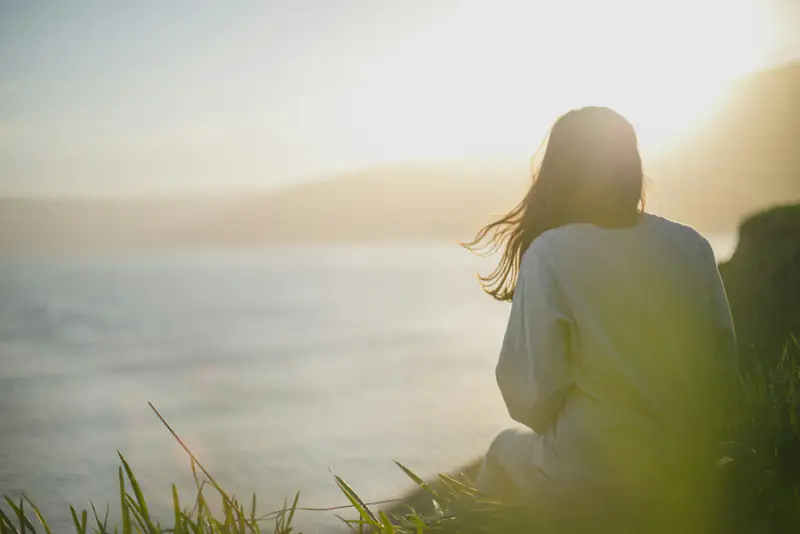Breathing exercise for stressful moments A woman sitting quietly by the sea at sunrise, practising a calming breathing exercise